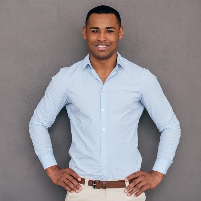 Confident young African man keeping arms crossed and looking at camera while standing against grey background