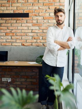 Young man entrepreneur looking at camera standing in small startup office